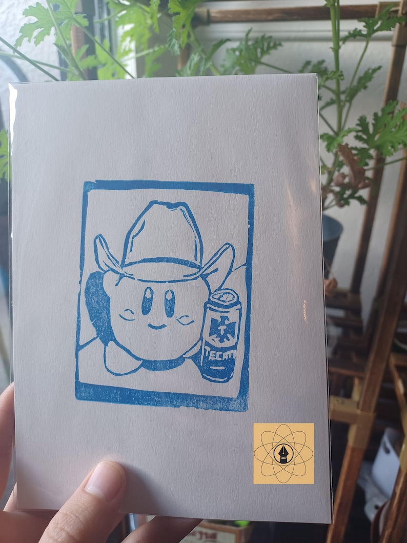 May include: A blue linocut print on white paper features a cartoon character wearing a cowboy hat and holding a can of Tecate beer. The print is framed in a blue rectangle. A small logo is in the bottom right corner.