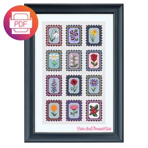 May include: Framed cross-stitch artwork with twelve floral postage stamp designs. Each stamp displays a different flower in various colours, set against a light blue background. The frame is dark blue, and the artwork includes the text "Cats And Threads Club".