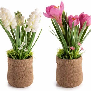 May include: Two potted artificial flower arrangements. One features white hyacinth flowers, the other has pink crocus blooms. Both are in woven brown fabric pots, with green foliage and small white and pink accent flowers.