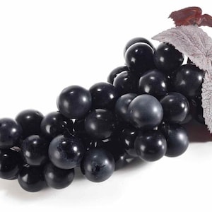 Puede incluir: Un racimo de uvas moradas oscuras con algunas hojas. Las uvas son redondas y brillantes, con un color profundo, casi negro. Las hojas son de un morado apagado y tienen una apariencia texturizada. Las uvas están dispuestas en una forma natural y orgánica.