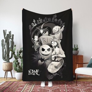 May include: Black and white throw blanket featuring characters from The Nightmare Before Christmas. The design includes Jack Skellington, Sally, and other characters, with a graveyard scene and the word "NAME" in a stylized font.