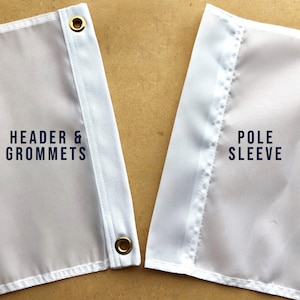 Op de afbeelding: Close-up van een witte vlag met een header en grommets aan de linkerkant en een paalhoes aan de rechterkant. De vlag heeft een witte rand en gouden grommets. Tekst op de vlag luidt "HEADER & GROMMETS" en "POLE SLEEVE".