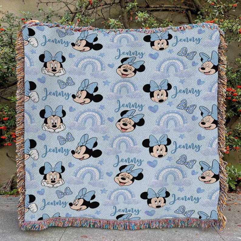 May include: A light blue throw blanket featuring a repeating pattern of Minnie Mouse, bows, rainbows, and stars. The name "Jenny" is written in a script font throughout the design. The blanket has a fringed edge.
