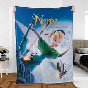 May include: A blue blanket featuring a cartoon fairy in a green dress, holding a staff, with a glowing firefly. The blanket has the word "Name" in gold script. The background is a blue sky with a large moon.