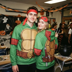 May include: Two green hooded sweatshirts featuring a printed brown turtle shell pattern on the front and back, red arm bands, and a brown belt with an R buckle. One person wears a red headband, and the other wears a red eye mask with a metal sai.