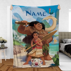 May include: A large, rectangular blanket with a vibrant illustration of characters from the animated film Moana. The design features Moana, Maui, Pua, and Hei Hei, set against a tropical beach and ocean backdrop. The word "Name" is written in blue.
