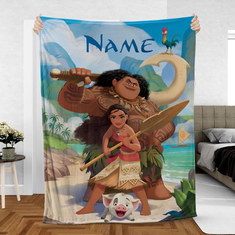 May include: A large, rectangular blanket with a vibrant illustration of characters from the animated film Moana. The design features Moana, Maui, Pua, and Hei Hei, set against a tropical beach and ocean backdrop. The word "Name" is written in blue.