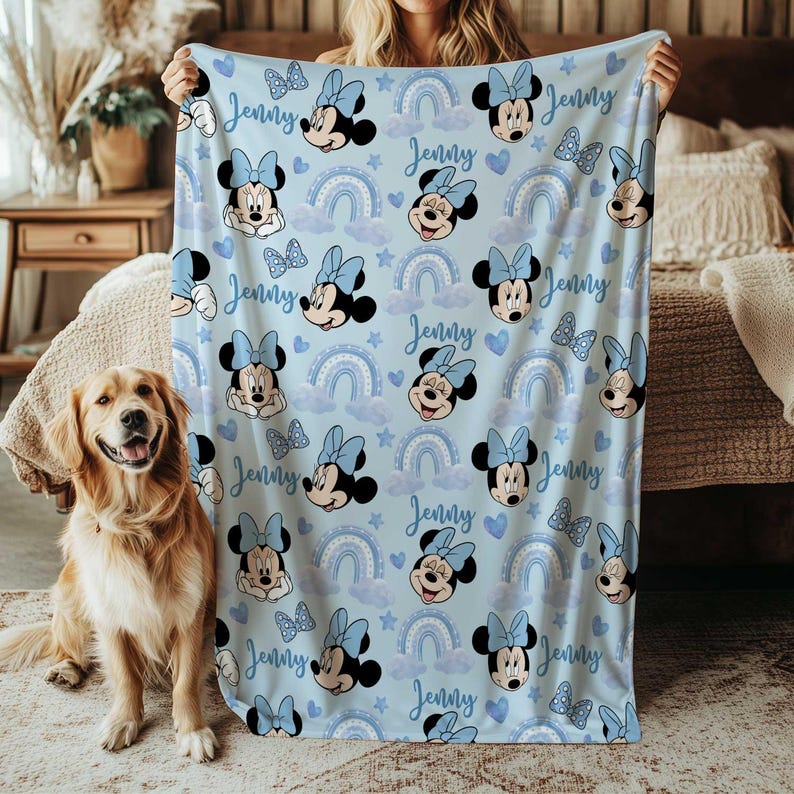 May include: A light blue blanket featuring a pattern of Minnie Mouse, bows, rainbows, clouds, and stars. The name "Jenny" is written in cursive throughout the design. A golden retriever dog is sitting on the left side of the image.