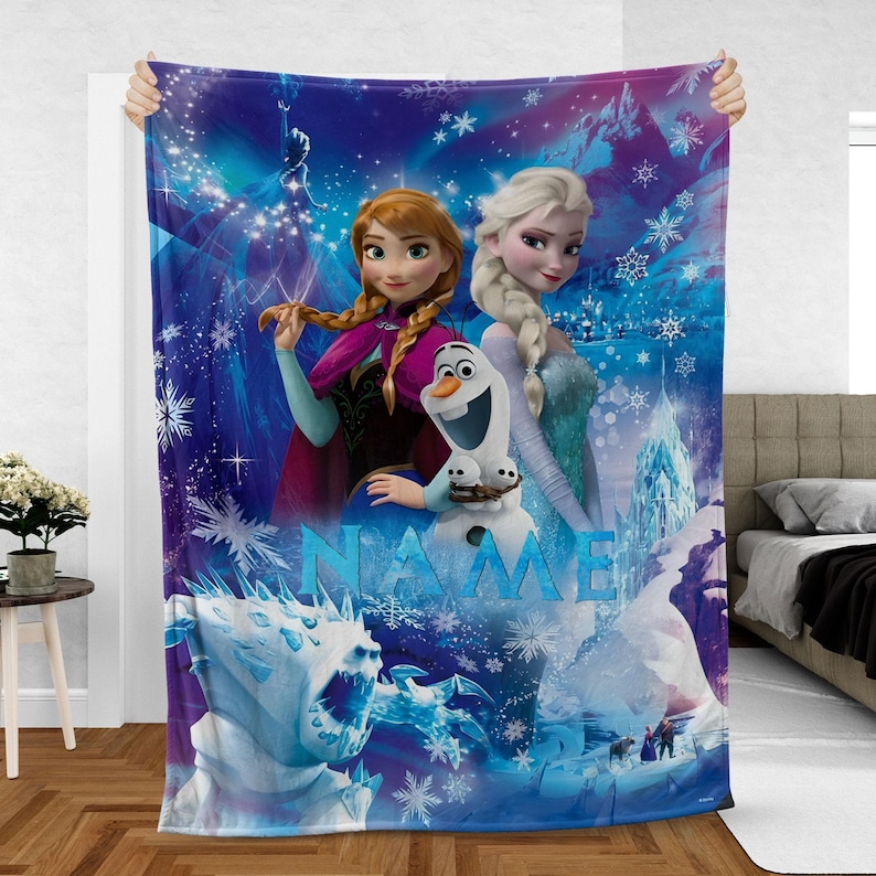 May include: A blue and purple fleece blanket featuring characters from the movie Frozen. The blanket displays Anna, Elsa, Olaf, and a snow monster, with the word "NAME" in large blue letters. Snowflakes and a castle are also visible.