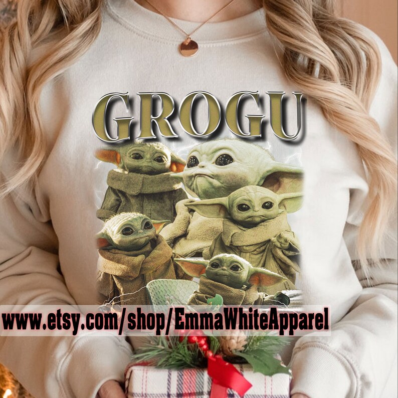 May include: A white sweatshirt with a graphic print of multiple Baby Yoda characters from the Star Wars series. The text "GROGU" is printed in gold above the characters. The text "www.etsy.com/shop/EmmaWhiteApparel" is printed below the characters.