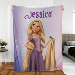 May include: A personalized blanket featuring a cartoon illustration of a princess with long blonde hair, wearing a purple dress, and holding a green frog. The name "Jessica" is written in a cursive font at the top of the blanket. The background transitions from purple to blue.