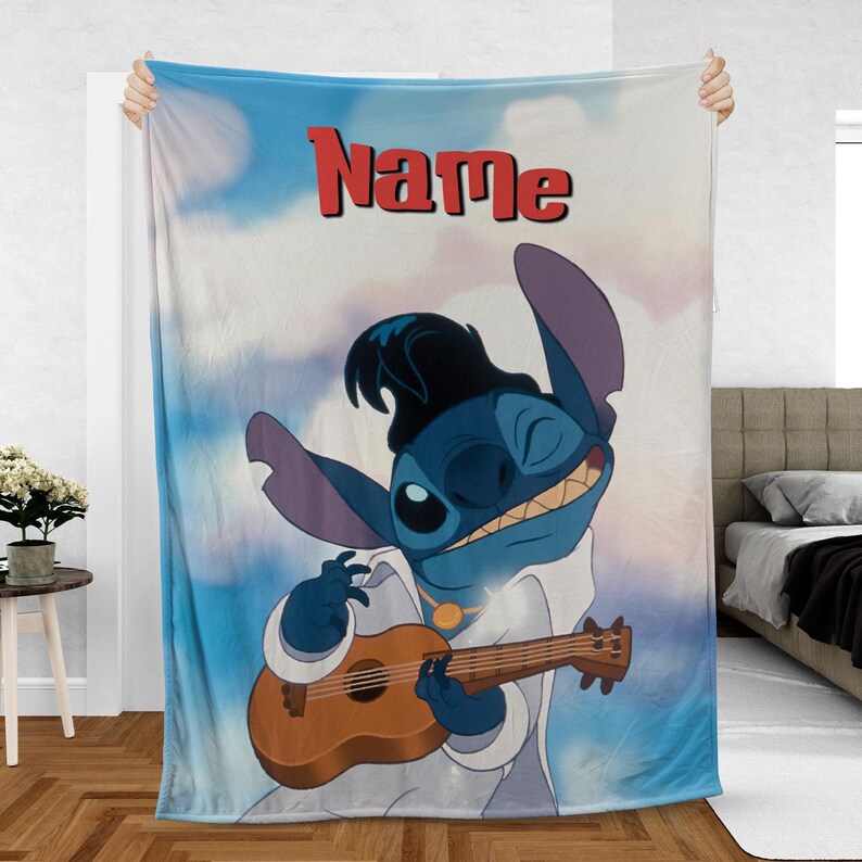 May include: A blue and white blanket featuring a cartoon character playing a ukulele. The character is wearing a black wig and white outfit. The word "Name" is written in red across the top of the blanket.