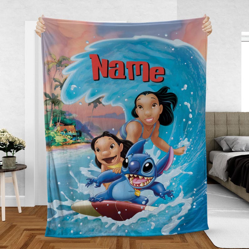 Op de afbeelding: Een zachte deken met een kleurrijke illustratie van Lilo & Stitch die op een golf surfen. De deken toont de personages Lilo, Nani en Stitch, met het woord "Name" in het rood. De achtergrond toont een tropische strandsc&egrave;ne met palmbomen en zonsondergang.