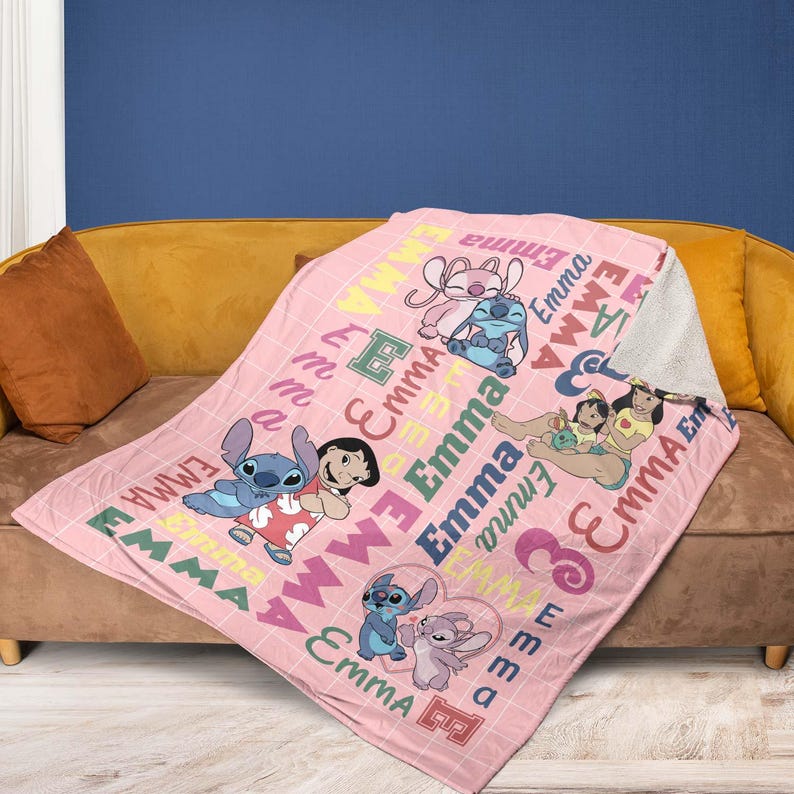 May include: Pink fleece blanket featuring cartoon characters and the name "Emma" in various colors. The blanket has a grid pattern and images of Stitch and Angel.
