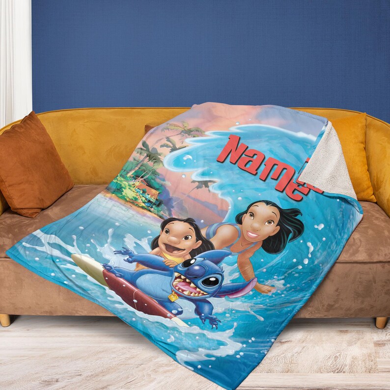 Op de afbeelding: Een blauw-witte deken met een cartoonsc&egrave;ne met de personages Lilo, Stitch en Nani die surfen. De deken heeft een zachte, pluche textuur en het woord "Name" in het rood.