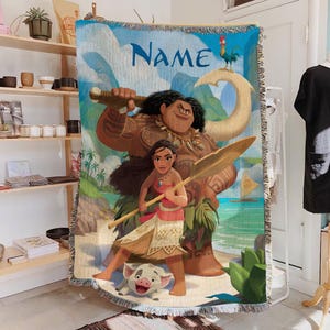 May include: A woven throw blanket with a vibrant illustration of characters from a popular animated film. The design includes a large figure holding a weapon, a female character with a spear, and a small pig. The word "Name" is written in large blue letters.