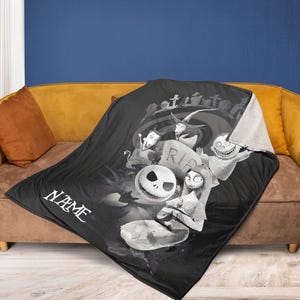 May include: Black throw blanket featuring characters from The Nightmare Before Christmas. The blanket has a white sherpa lining and a graphic of Jack Skellington, Sally, and other characters. The word "NAME" is printed on the blanket.