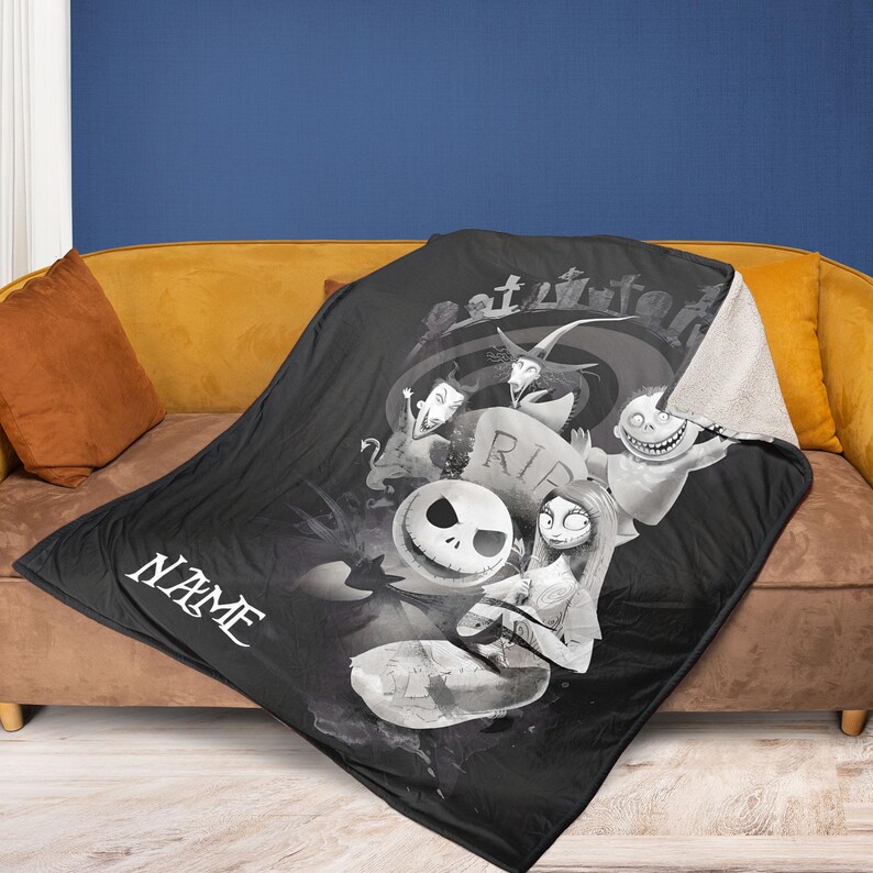 May include: Black throw blanket featuring characters from The Nightmare Before Christmas. The blanket has a white sherpa lining and a graphic of Jack Skellington, Sally, and other characters. The word "NAME" is printed on the blanket.