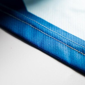 Puede incluir: Primer plano de una tela azul con costuras blancas. La tela tiene una superficie texturizada.