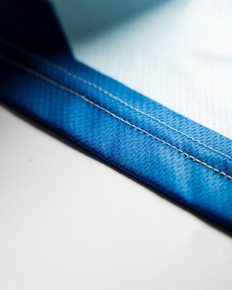 Puede incluir: Primer plano de una tela azul con costuras blancas. La tela tiene una superficie texturizada.