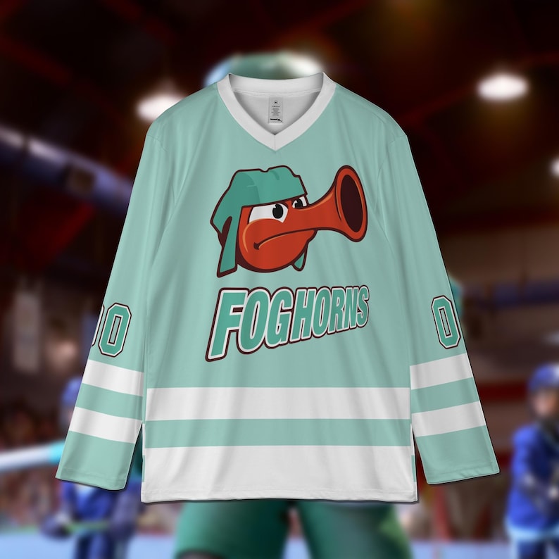 Puede incluir: Una camiseta de hockey de color turquesa con rayas blancas y un personaje de dibujos animados con la cara roja y un sombrero verde que toca una bocina. La camiseta tiene el texto "FOGHORNS" impreso en la parte delantera.