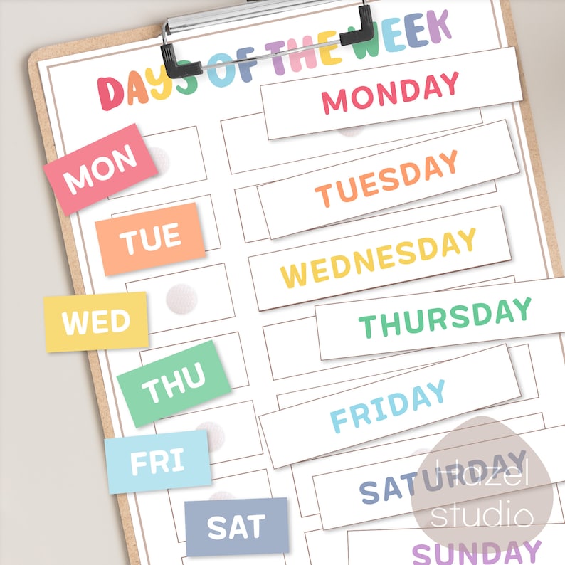 May include: A printable chart with the days of the week written in colorful text. The days of the week are written in a rainbow color scheme. The chart is on a clipboard.