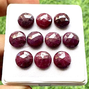 以下が含まれることがあります： 白いディスプレイボックスに入った、丸くてファセットカットされたルビーの宝石が9つ。ルビーは濃い赤色で、研磨された仕上げになっています。