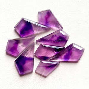 May include: A group of seven purple amethyst gemstone cabochons, each cut into a sharp, pointed shape. The stones are translucent and have a variety of purple hues.