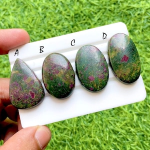 Op de afbeelding: Vier gepolijste edelstenen met een mix van groen en bordeauxrood. De edelstenen liggen op een wit oppervlak, met de letters A, B, C en D. De achtergrond is een wazig groen.