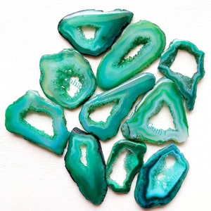 May include: A collection of polished agate slices in shades of green and teal. Each slice has a unique shape and a crystalline center, showcasing natural patterns. The stones vary in size and are arranged on a white surface.