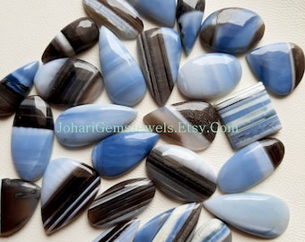 May include: A collection of polished blue and brown banded opal cabochons in various shapes including teardrop, oval, and square. The stones feature smooth, glossy surfaces with distinct horizontal and vertical stripes. Text reads JohariGemsjewels.Etsy.Com.