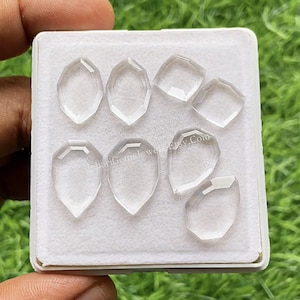 Op de afbeelding: Een verzameling van zeven heldere, gefacetteerde, schildvormige edelstenen gerangschikt op een witte schuiminzet in een vierkante houder. De stenen zijn transparant en kleurloos met geometrische slijpvormen. De tekst JohariGemsJewelry.Etsy.Com is zichtbaar.