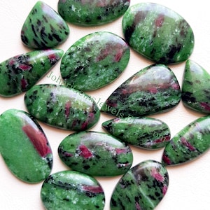 May include: A collection of polished ruby in zoisite gemstones. The stones are a vibrant green with black and red inclusions, in various oval and teardrop shapes. The gemstones are smooth and reflect light.