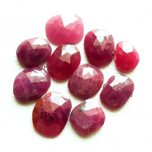 May include: Ten faceted ruby gemstones in various shades of red, ranging from light pink to deep red. The stones are all cut in a similar oval shape and have a polished finish.
