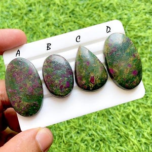 Peut inclure: Quatre pierres précieuses polies avec un mélange de teintes vertes et rouges. Les pierres sont de forme ovale et en goutte, chacune avec un motif unique. Les pierres sont présentées sur une surface blanche sur fond d'herbe verte.