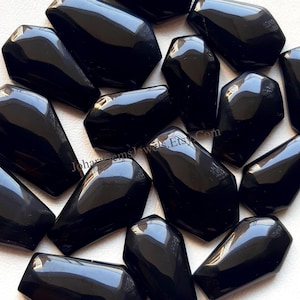 Peut inclure: Collection de pierres précieuses en obsidienne noire polie. Chaque pierre a une surface lisse et réfléchissante et une forme allongée unique. Les pierres sont disposées de près, remplissant le cadre.