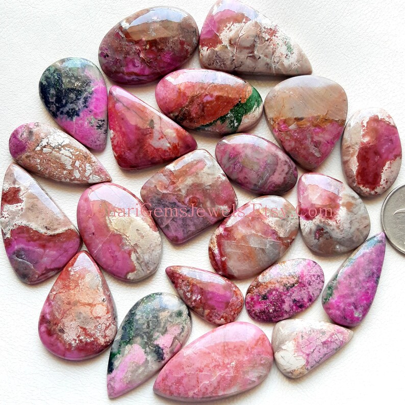 May include: A collection of 20 pink, brown, and green gemstone cabochons. The cabochons are various shapes and sizes, with a polished, smooth finish.