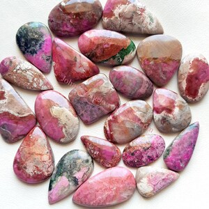 May include: A collection of 18 pink, red, and green gemstone cabochons. The cabochons are various shapes and sizes, with a polished, smooth surface.