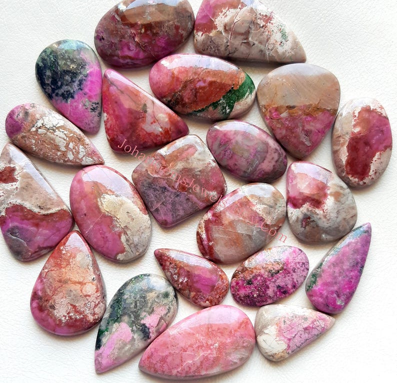May include: A collection of 18 pink, red, and green gemstone cabochons. The cabochons are various shapes and sizes, with a polished, smooth surface.