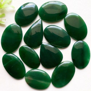 Könnte beinhalten: Eine Sammlung von 12 grünen Achat-Cabochons, jeder mit einer einzigartigen Form und einem einzigartigen Muster. Die Cabochons sind glatt und poliert und haben eine tiefgrüne Farbe.