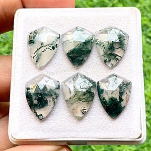May include: Six shield-shaped moss agate gemstones arranged in two rows of three. Each translucent stone features a faceted top surface and distinct dark green, branch-like dendritic inclusions suspended within the clear, pale white quartz base.