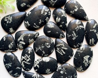 May include: A collection of polished black chrysanthemum stone cabochons featuring white, flower-like crystalline patterns. The stones are shaped in various ovals, teardrops, and triangles, displaying a smooth, reflective surface texture throughout.