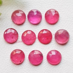 Puede incluir: Nueve piedras preciosas rosas, redondas y facetadas, dispuestas en tres filas. Cada piedra presenta una superficie de talla rosa con múltiples facetas triangulares que reflejan la luz. Las piedras muestran un tono rosa vibrante y translúcido.