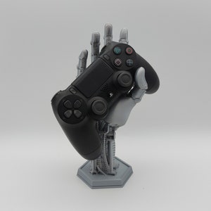 Controller Halter im Roboter-Hand Design. Farbe Silber. Es liegt ein Playstation Controller auf der Hand