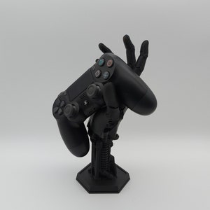 Controller Halterung im Alien-Hand Design. Farbe Schwarz. Es liegt ein PS5 Controller auf der Hand. Science Fiction Stil