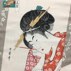 May include: Japanese woodblock print featuring a woman in a red floral kimono, writing with a brush. Her hair is styled with decorative pins. The print includes Japanese text and a fan illustration. The background is a light gray with floral patterns.