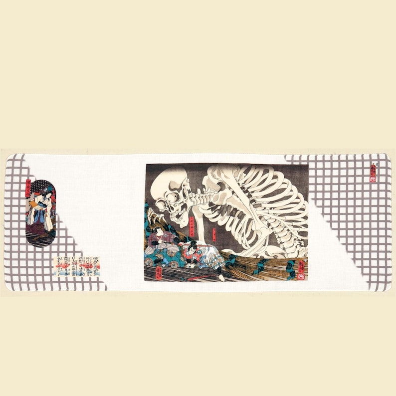 May include: A rectangular, white decorative mat with a Japanese-style print. The print features a large skeleton and figures in traditional clothing. The mat has a gray checkered pattern on the edges and a smaller print on the left side.