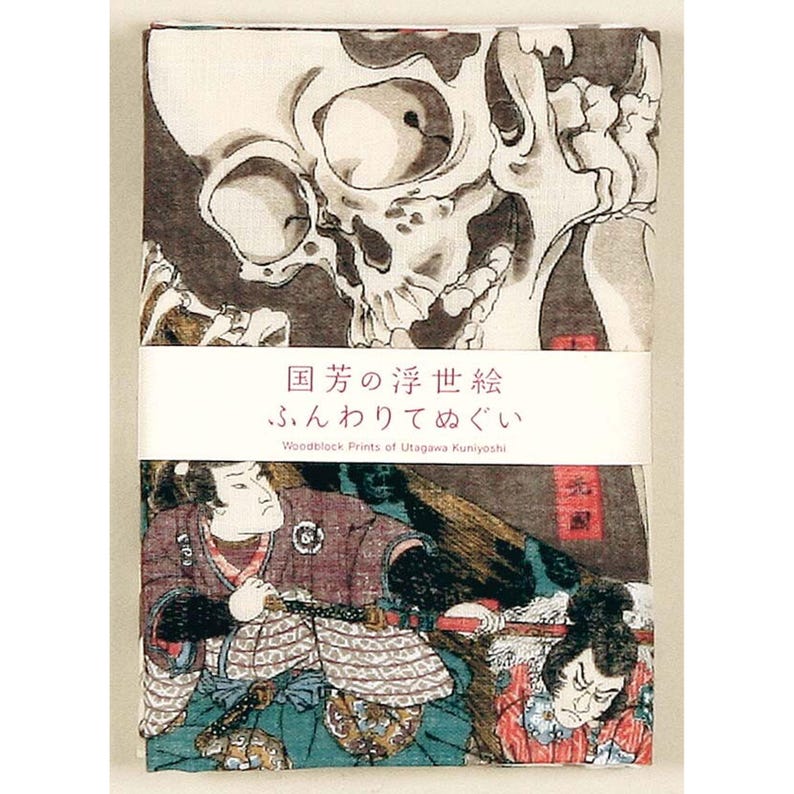 May include: A folded cloth featuring a Japanese woodblock print design. The top half displays a detailed skull illustration in black and gray. The bottom half shows a scene with two figures in traditional attire. Text in Japanese and English is visible.