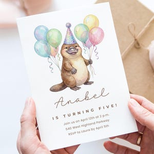 May include: A birthday invitation featuring a watercolor illustration of a platypus wearing a party hat and holding colorful balloons. The invitation reads "Anabel is turning five!" with event details.