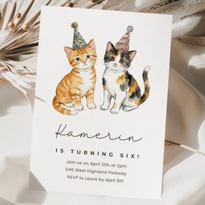 Puede incluir: Una tarjeta de invitación blanca con una ilustración en acuarela de dos gatitos con sombreros de fiesta. El texto "Kamerin IS TURNING SIX!" se muestra en una fuente manuscrita, junto con los detalles del evento. Los gatitos atigrados naranjas y calicó son el punto focal.